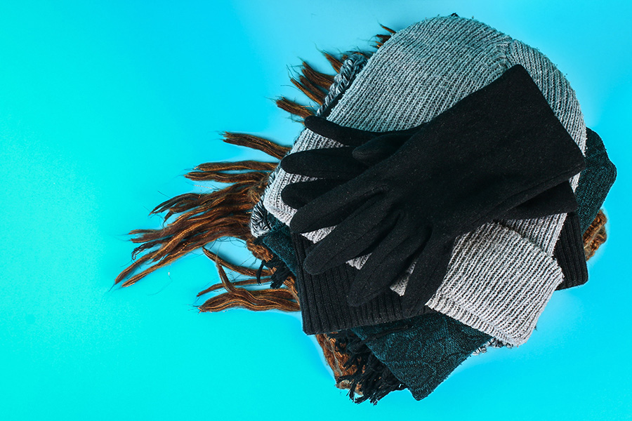 Neat stack of winter hats, scarves and gloves in various colors on bright blue background