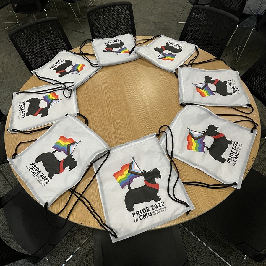 Table arranged with white tote bags printed with CMU Scotty logo carrying a Progress Pride flag 