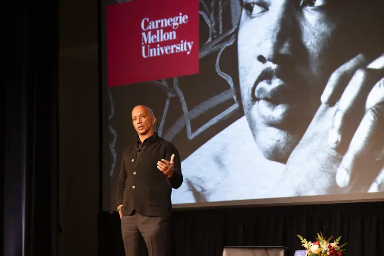 Byron Pitts on stage in front of big screen displaying image of MLK and CMU logo