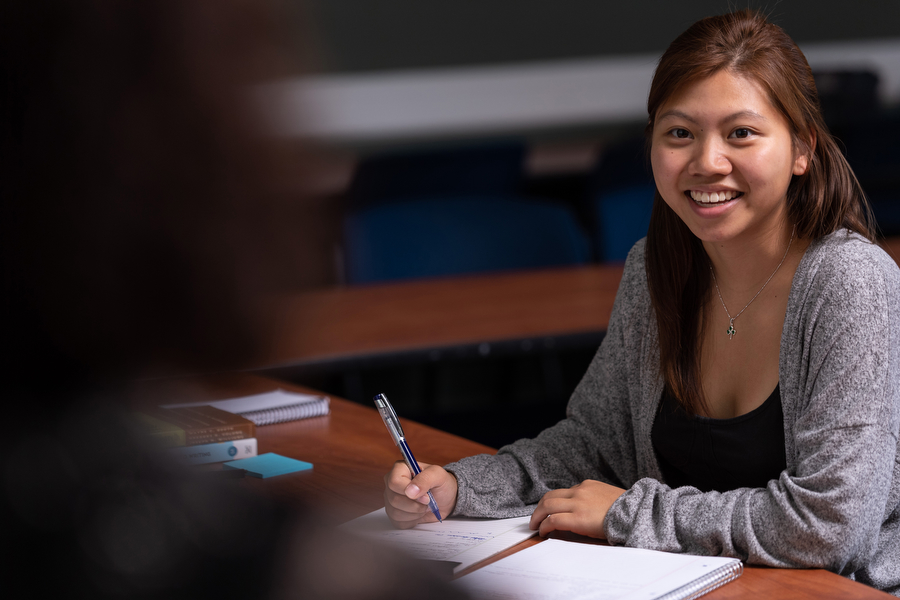 student smiling while at desk writing
