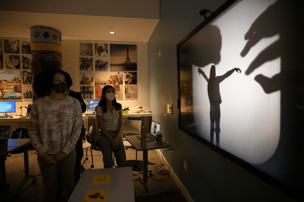 Students stand watching a screen that displays a projection of shadows