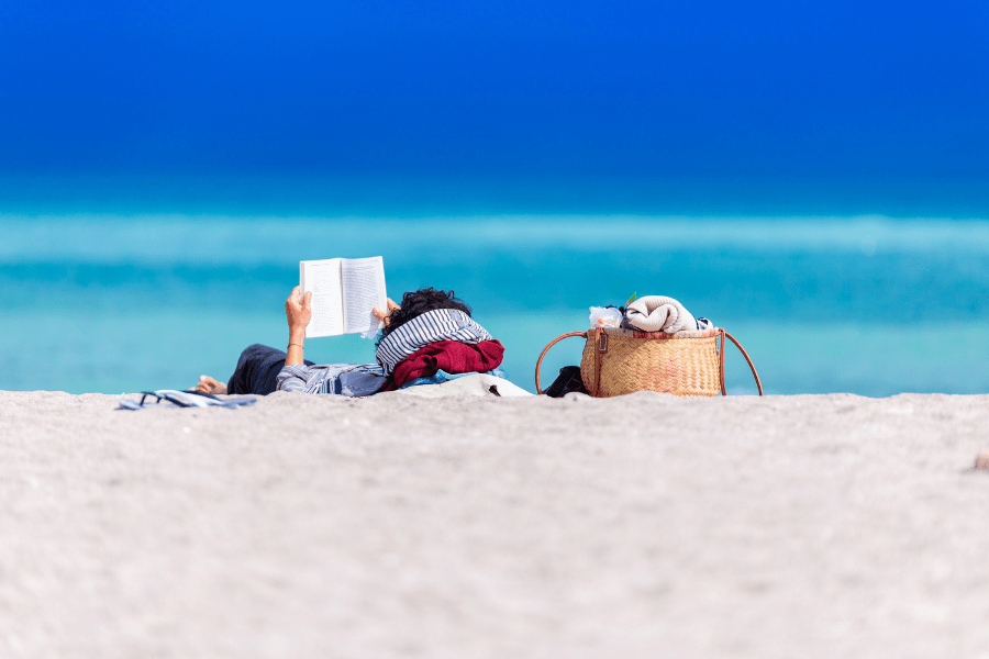 Woman lying down reading a book on the beach