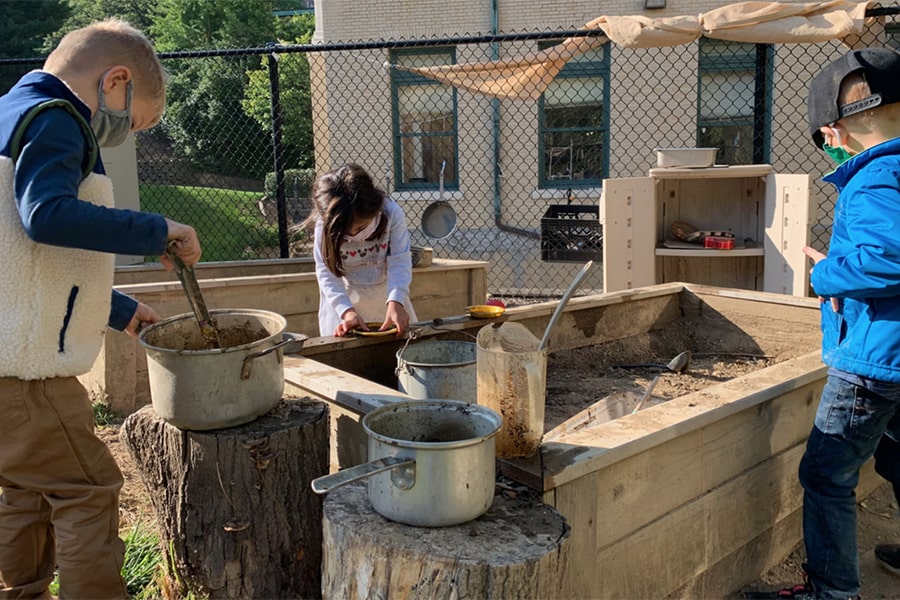 Children wearing masks, playing in the mud kitchen