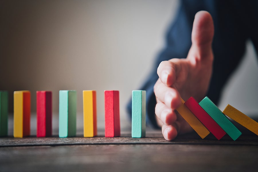 a line of colorful dominos with a hand in the middle stopping some from falling