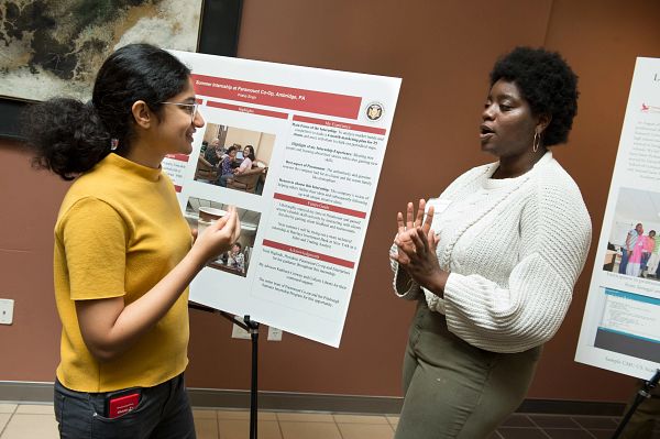 One student presents a research poster to another.