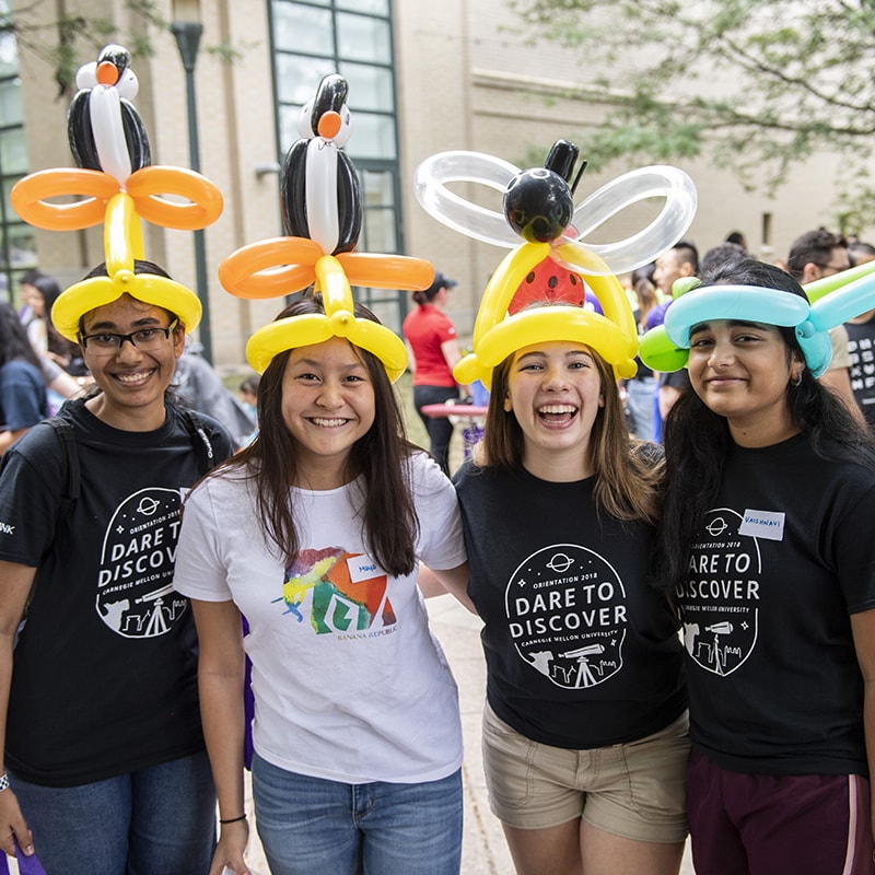 Photo of a group of four smiling students, wearing balloon hats
