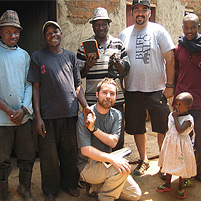 Before returning to the United States, Michael Taylor, kneeling, and Joshua Schapiro (standing, second from right), check on a family in Uganda. The family was using the device they developed to remove indoor air pollution from their hut.
