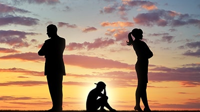 Silhouette image of a sad child sitting between two standing adults not looking at each other