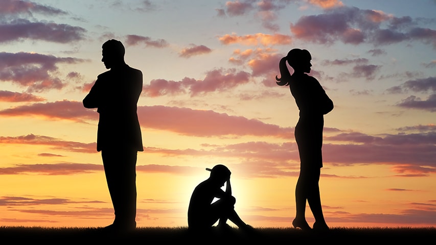 Silhouette image of a sad child sitting between two standing adults not looking at each other