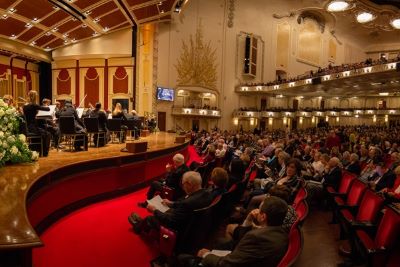 Image of a symphony on stage and a crowded audience