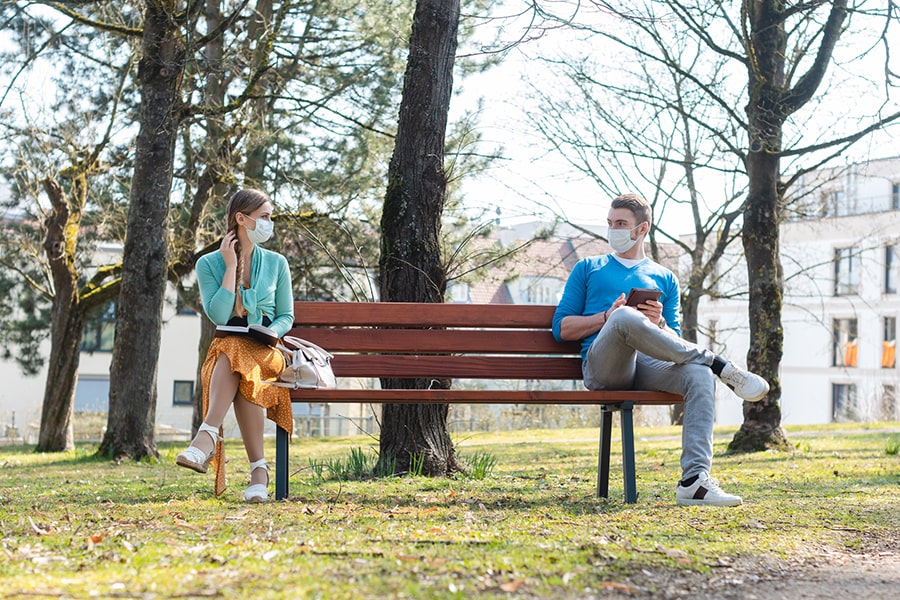 image of a man and woman wearing face coverings and social distancing on a park bench