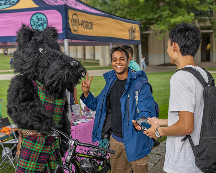 CMU students posing with Scotty mascot on a bike
