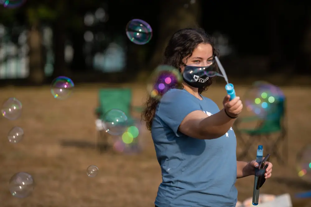 Student blowing bubbles with mask on.