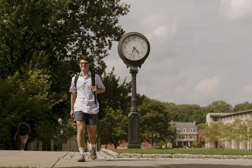 CMU student walking outside on campus in front of a large clock