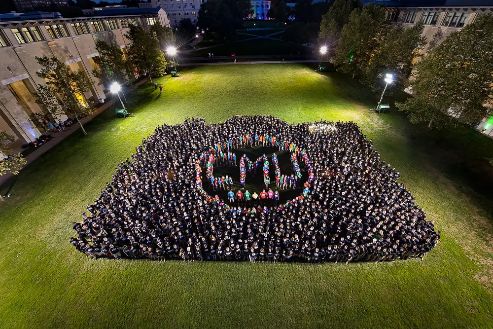 Large group of CMU students outside on campus at night forming together to make the letters "CMU"