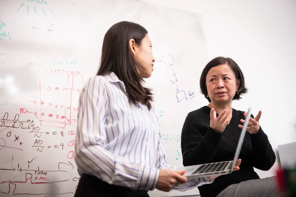 Student working with professor Wei Wu in front of a whiteboard with her laptop.