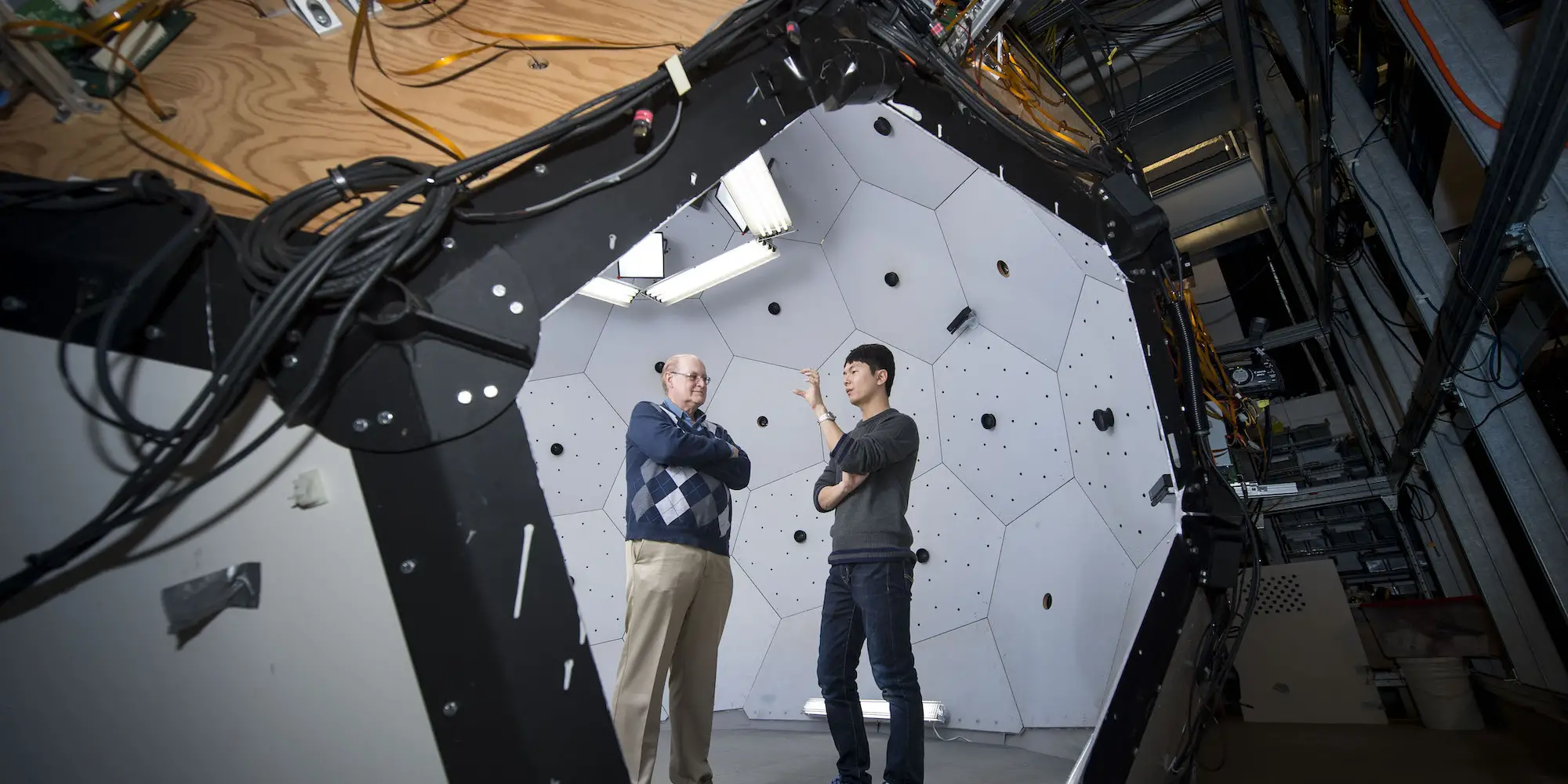 Student standing with professor, explaining something to him inside of a geodesic dome.