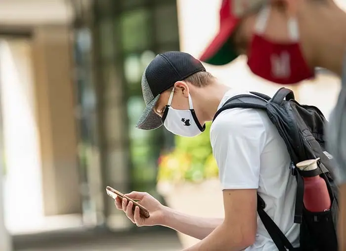 CMU student looking at phone wearing CMU Scotty branded mask