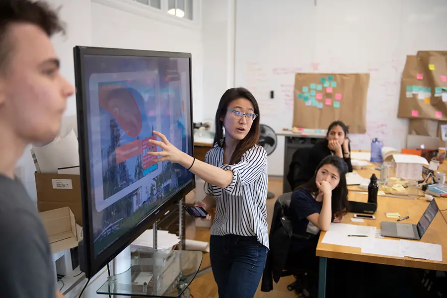 Student pointing to a screen, presenting to their class.
