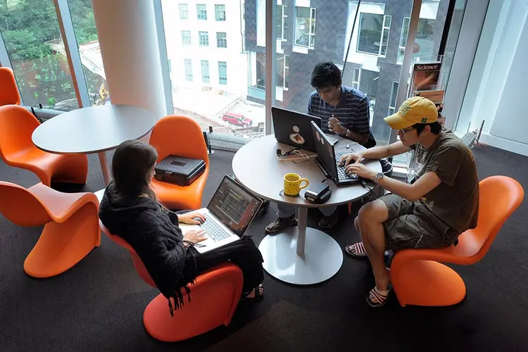 Students sitting on bright orange chairs, working from laptops.
