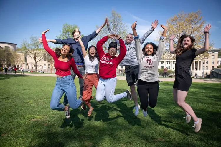 Students on the lawn jumping with hands in the air