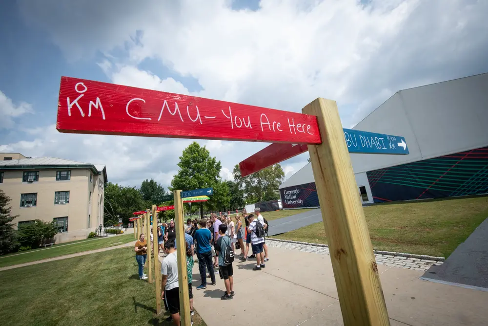 Signs on campus that point to different countries and include distance from them. The sign in focus says CMU You Are Here.