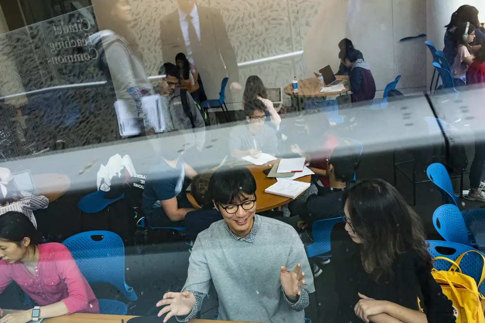 Looking through a window at students collaborating together in a common space.