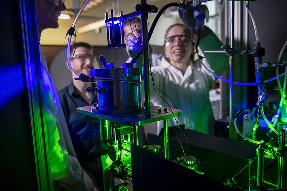 Students working in a lab with lab coat, goggles, and gloves.