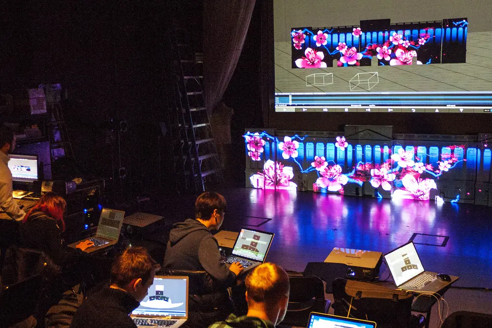 Students working from laptops as digital images are projected onto physical spaces.