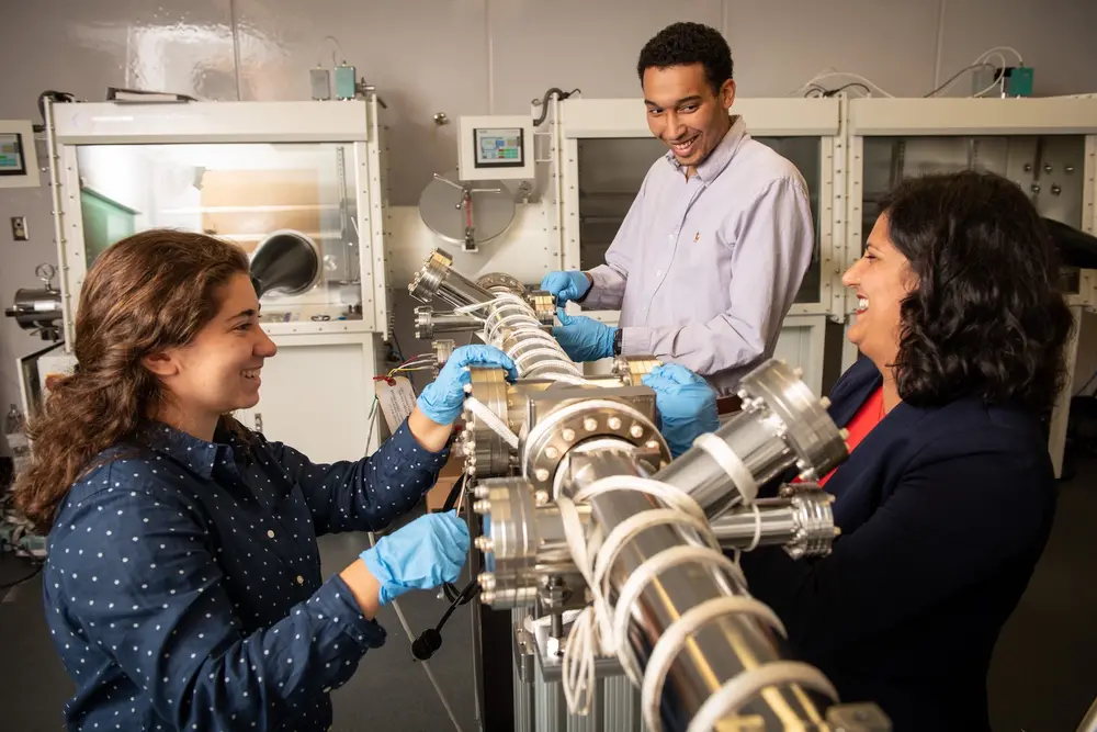 Students in a physics lab, working and smiling with professor Jyoti Katoch.