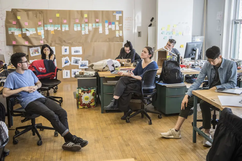 Design students collaborating in their studio, with Post-It notes covering the walls behind them.