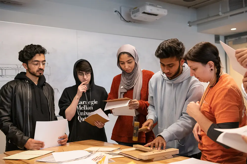 Students gathered around a table, referencing papers and a wooden model.
