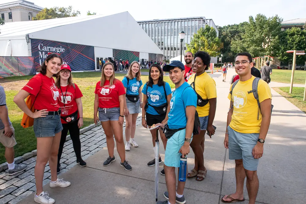 A diverse group of CMU students wearing colorful t-shirts and gathered outside on campus