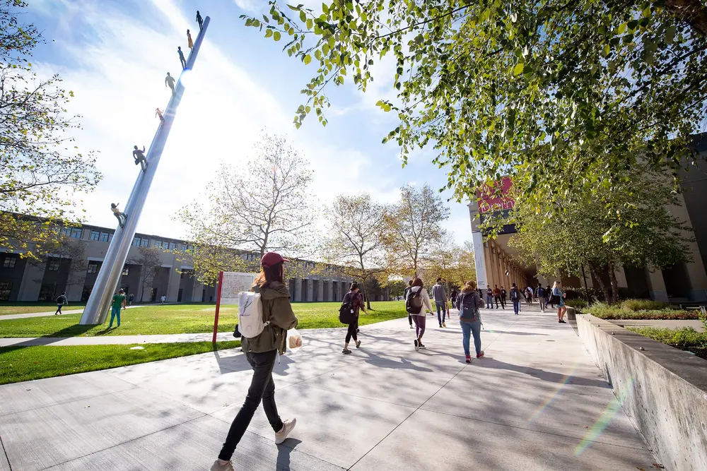 Students walking outdoors on CMU campus with the Walking to the Sky public sculpture by Jonathan Borofsky in the background