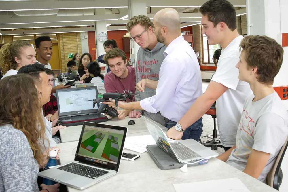 Students standing around a desk where a faculty member is showing a drone