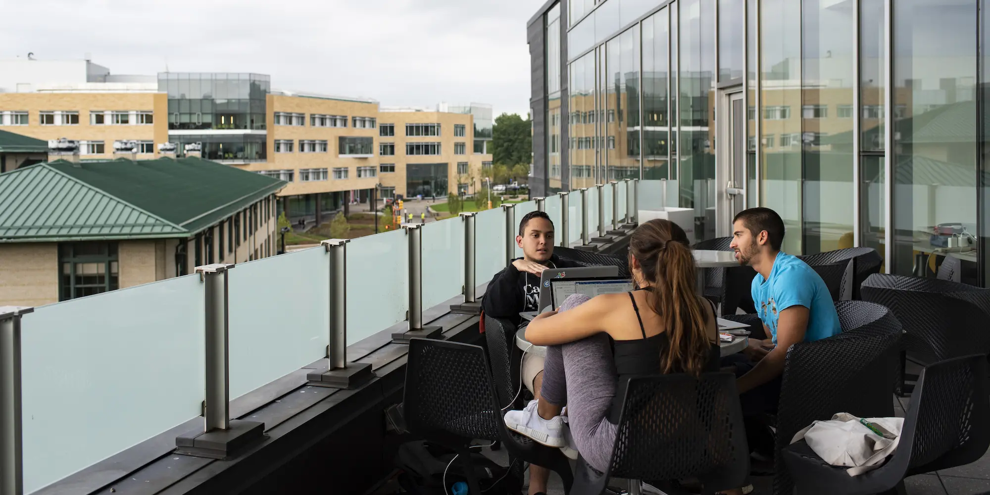 Students sitting on the balcony of the Tepper Quad, working from laptops.