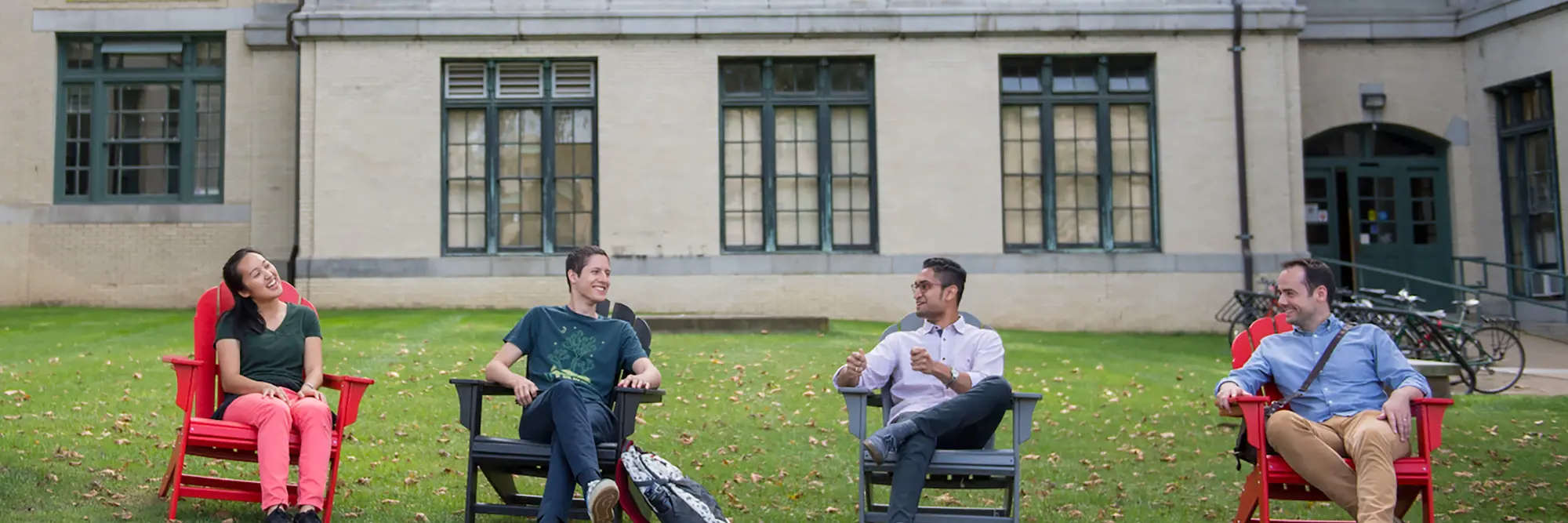 CMU students sitting and talking outside on campus on Adirondack chairs