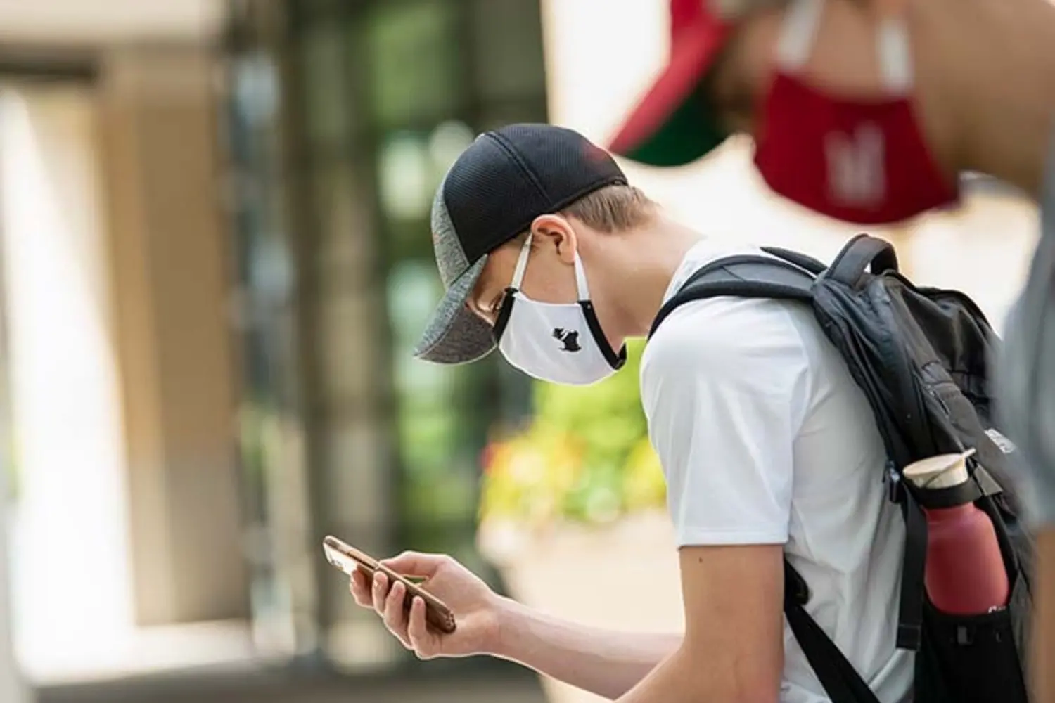 CMU student looking at phone wearing CMU Scotty branded mask