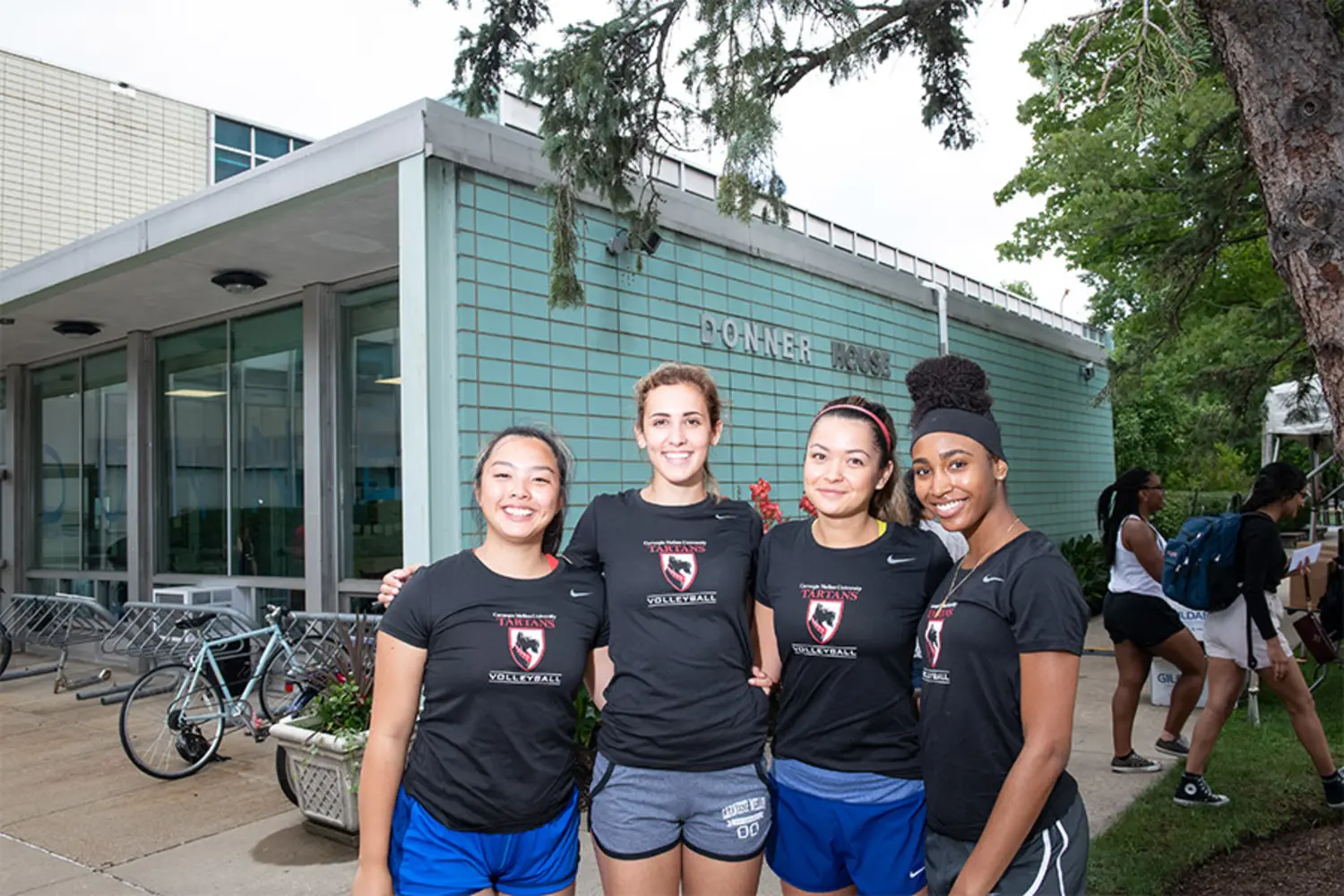Four student volleyball players standing outside of the Donner House dormitory.
