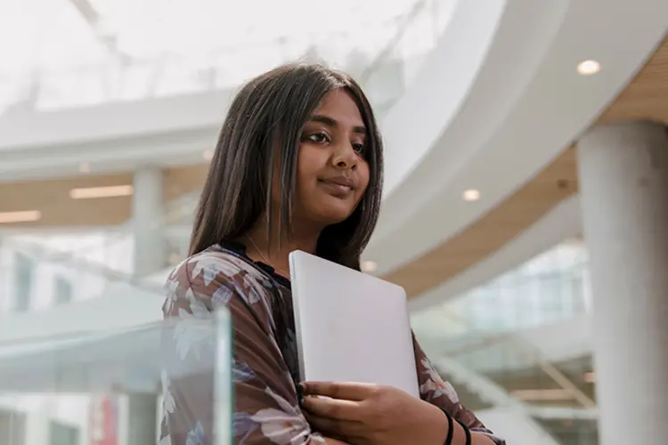 Student holding laptop, walking down the stairs.