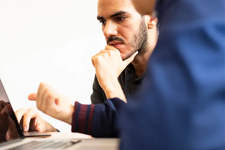 Student working with another, looking at a laptop.