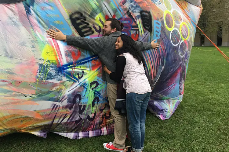 Two students hugging a large, inflatable soft sculpture art piece.