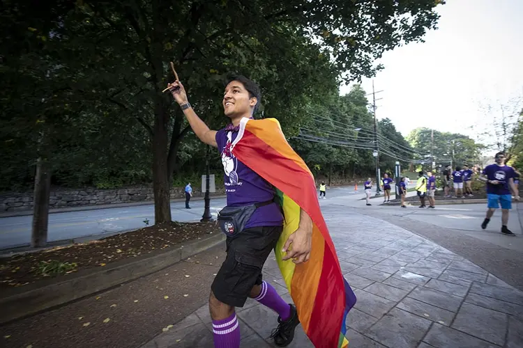 A student walking outside with a Pride flag on his back during CMU's Move In.