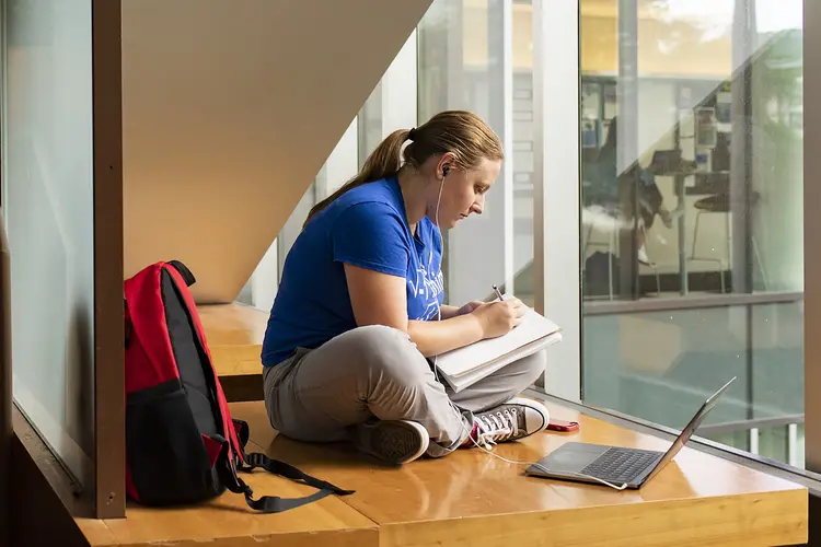 Student taking notes and working on laptop