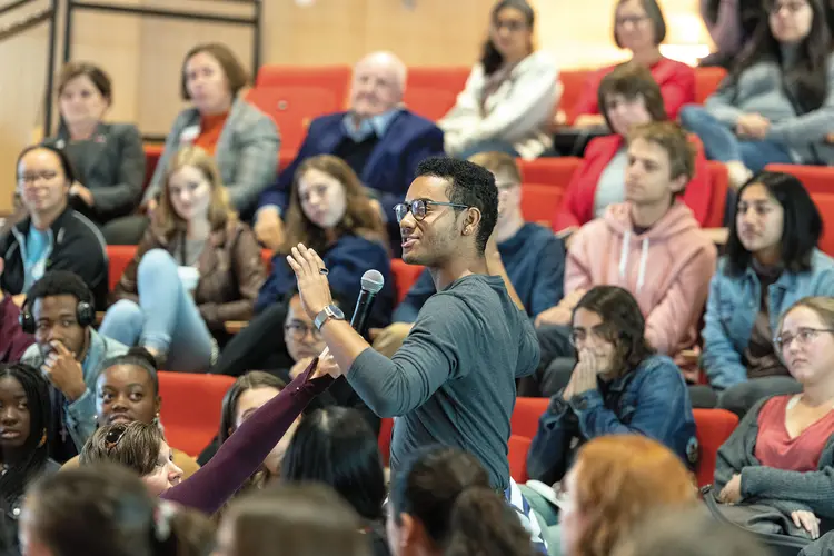 Student speaking in a lecture hall, surrounded by students listening.