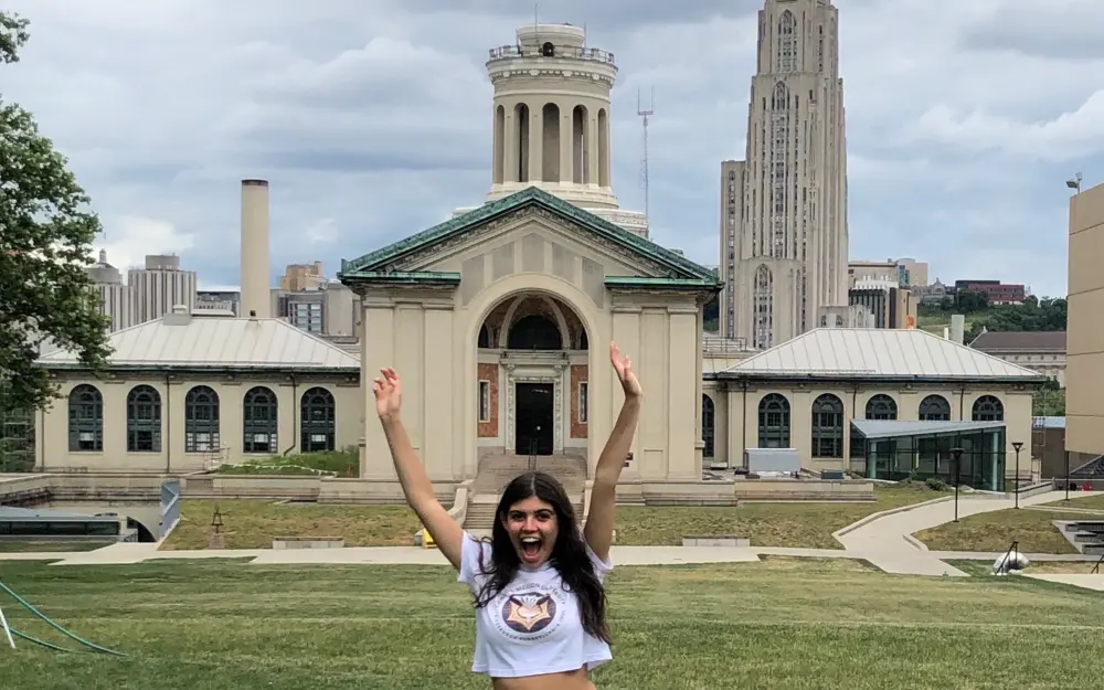 Student on campus smiling outside with arms up