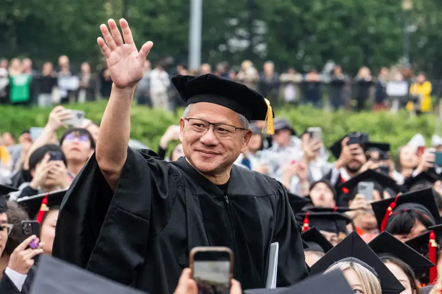 NVIDIA CEO Jensen Huang smiles and waves to an enthusiastic crowd of graduates holding up smartphones during the commencement ceremony outdoors.
