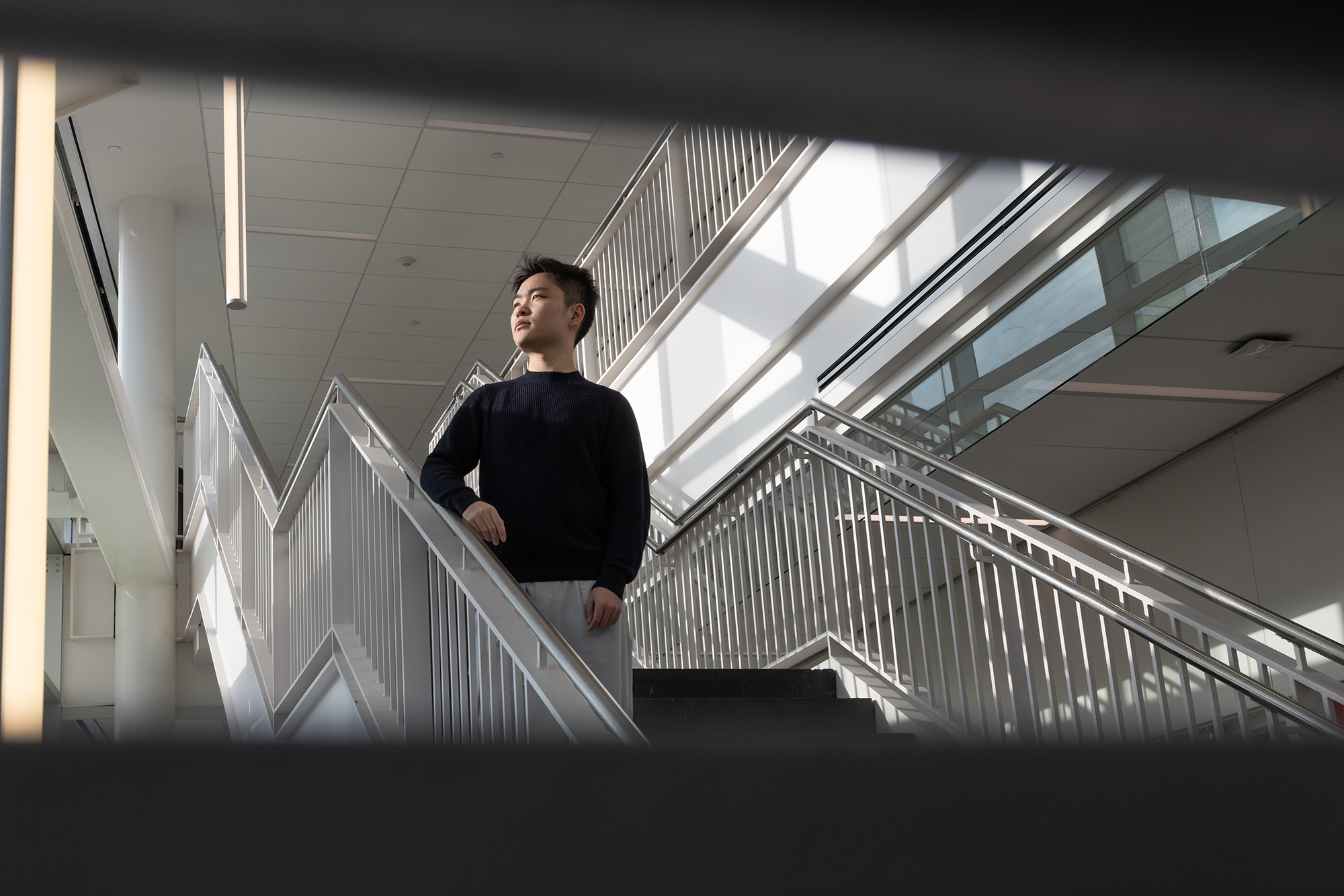 Zixi (Alan) Song stands on a white staircase and looks out a window.