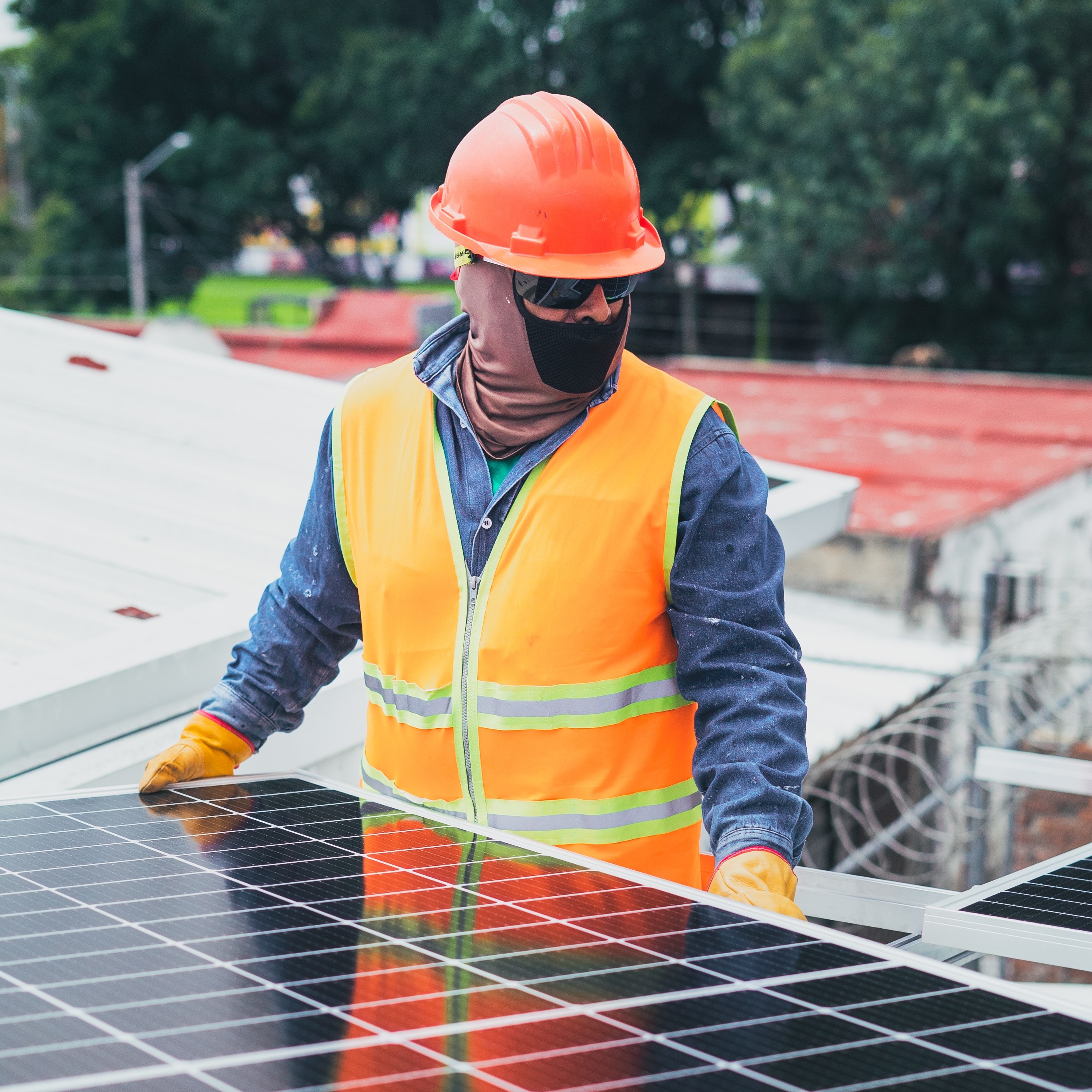 A worker in a reflective vest and hard hat carries a solar panel