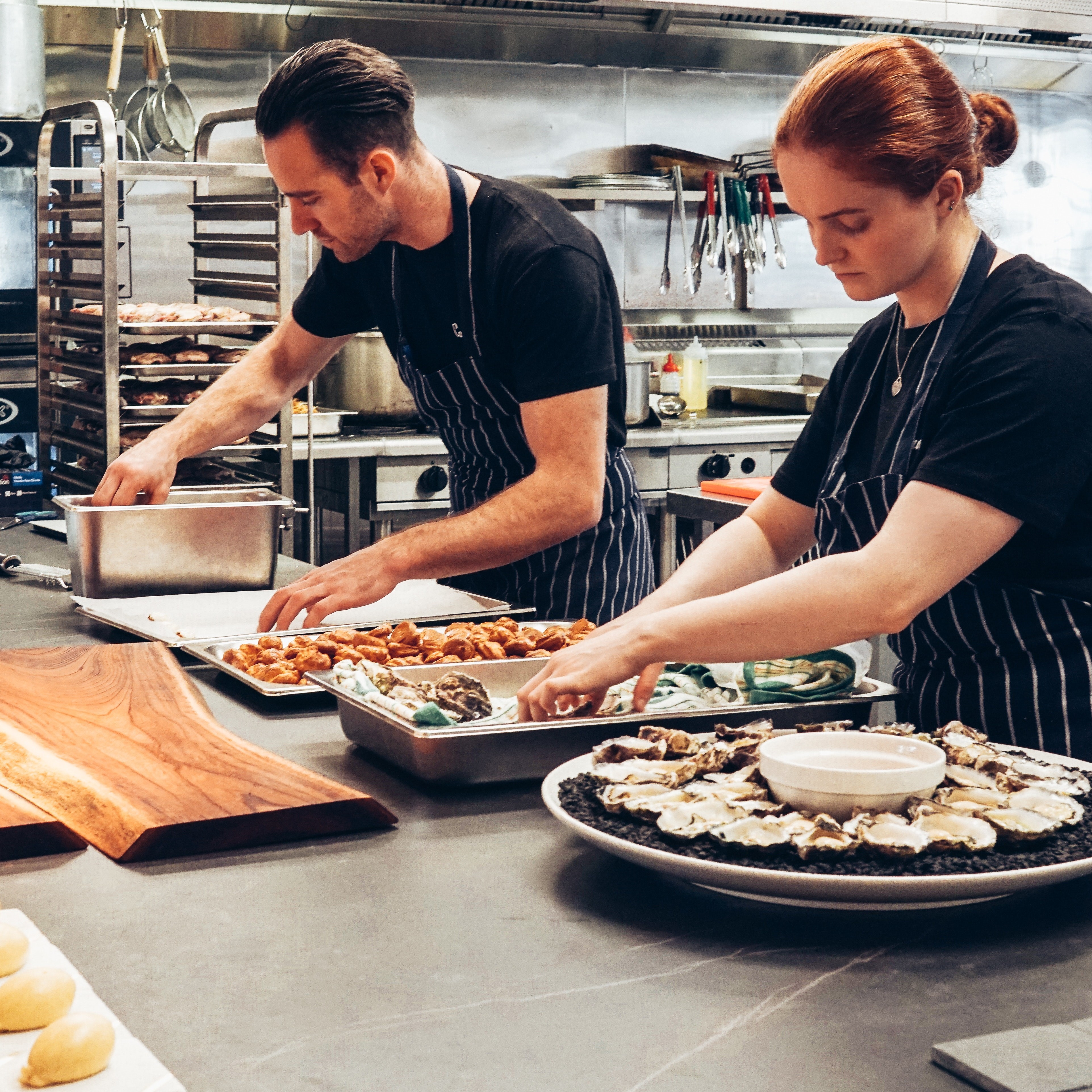 Two caterers prepare platters of food in industrial kitchen
